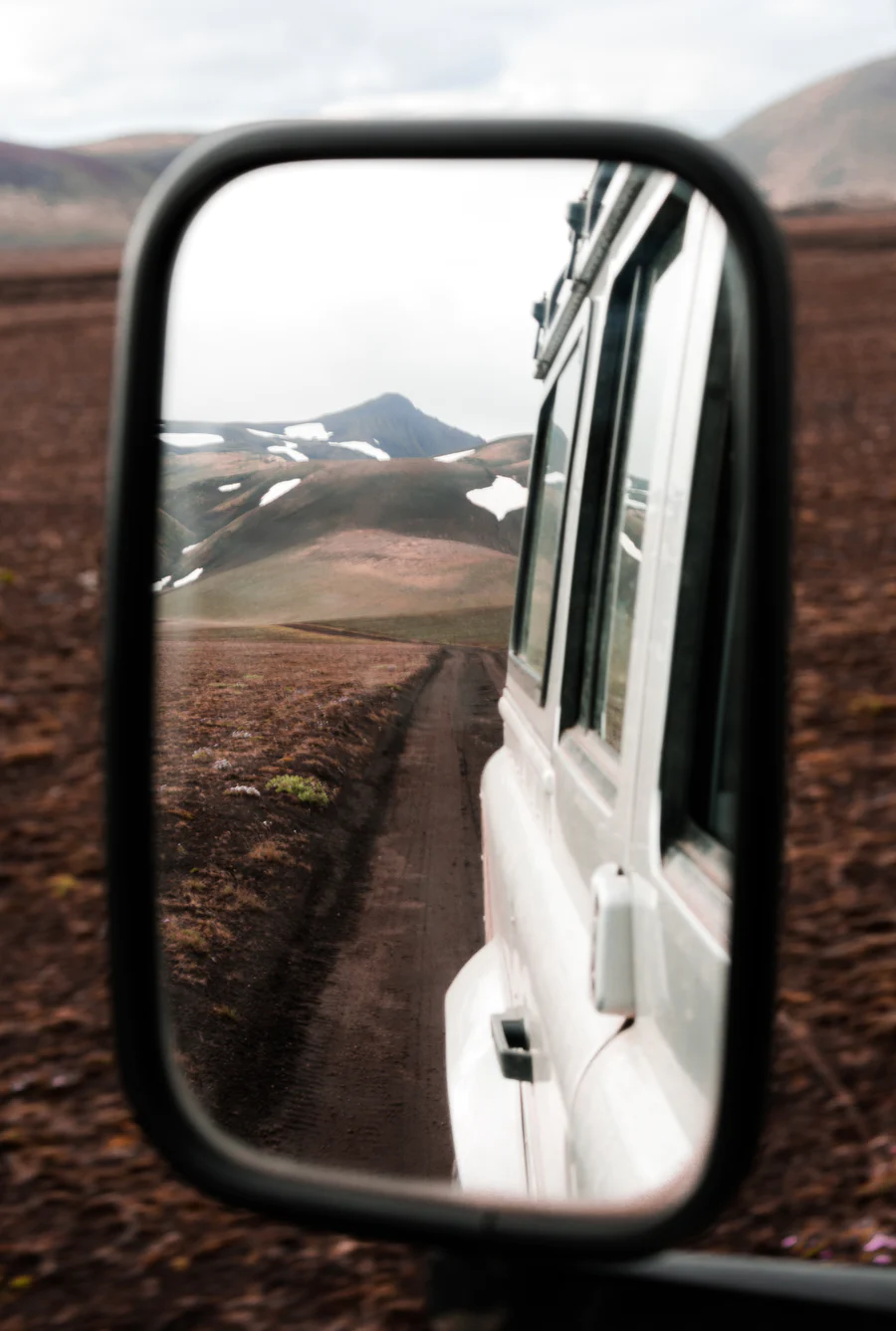 A view of the Icelandic Highlands from the wing mirror of a white 4x4 jeep vehicle