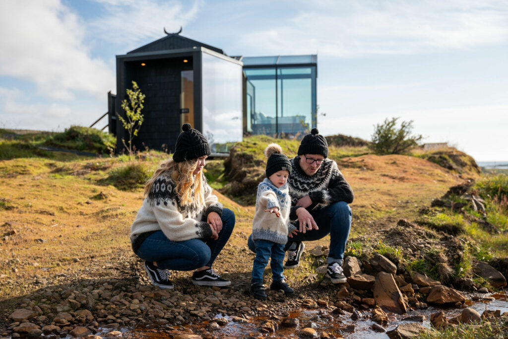 family in icelandic sweaters standing in front of panorama glass lodge