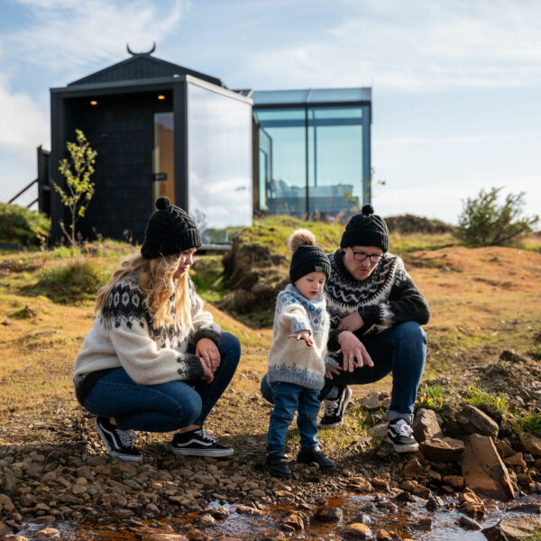 family in icelandic sweaters standing in front of panorama glass lodge